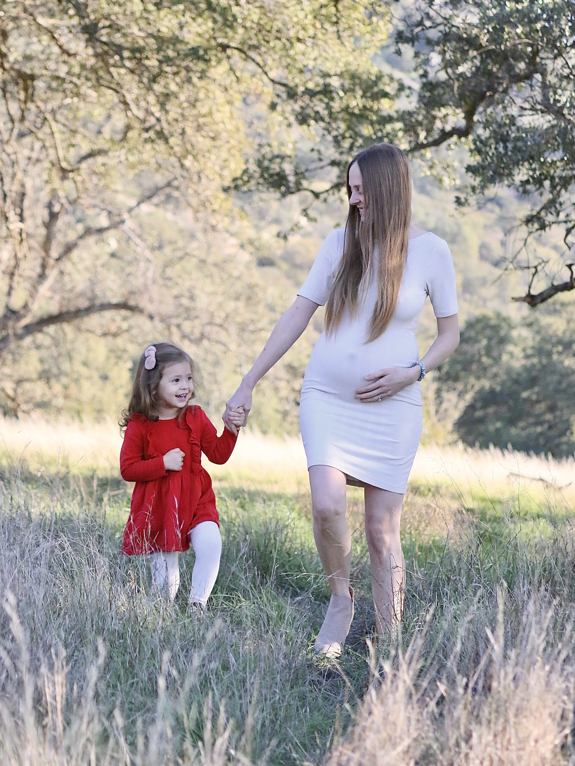 Mother and toddler walking together holding hands through a field of tall grass