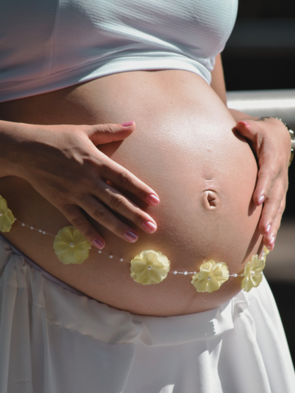 Pregnant woman is embracing her pregnant belly that has flowers draped on it