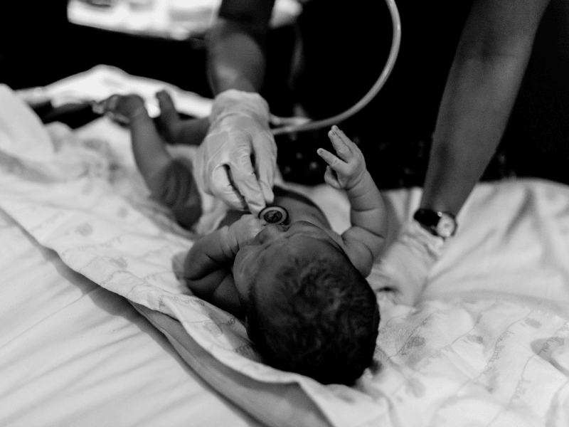 Midwife is taking a newborn’s vitals with a stethoscope on the bed