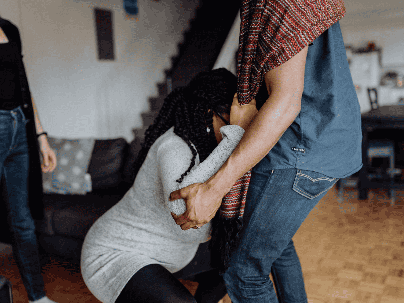A woman is laboring and is holding onto a rebozo that is wrapped around her husband as he supports her.